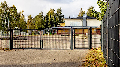 Koulun pihaan ympäröivään mustaan elementtiaitaan on tehty yhdistelmäportti, jossa on huoltoportti ajoneuvoille ja käyntiportti jalankulkijoille.